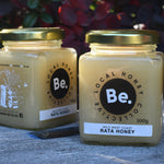 Two jars of honey from Be. Local Honey Company on a bee box with a blurred natural background.