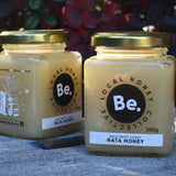 Two jars of honey from Be. Local Honey Company on a bee box with a blurred natural background.