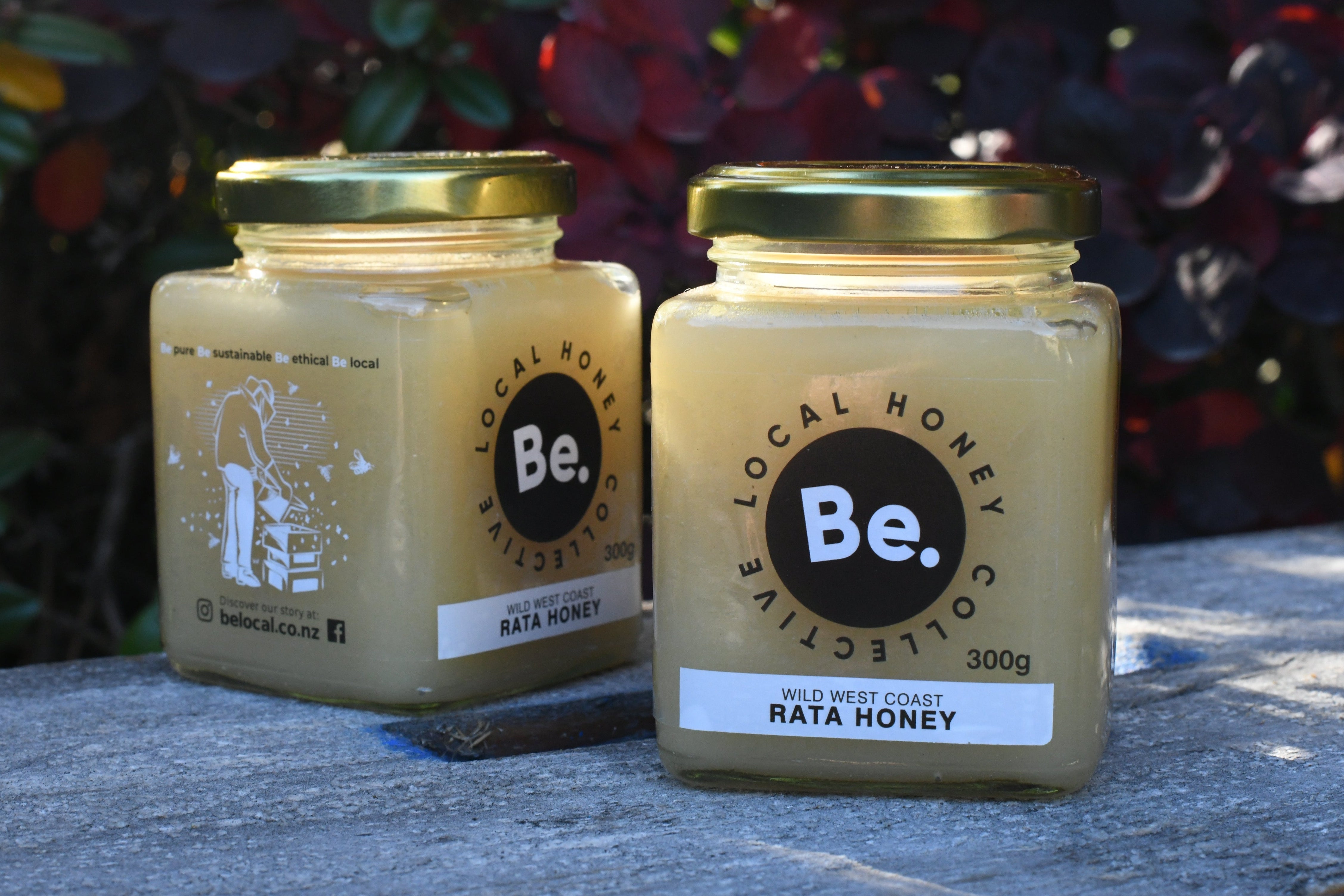 Two jars of honey from Be. Local Honey Company on a bee box with a blurred natural background.